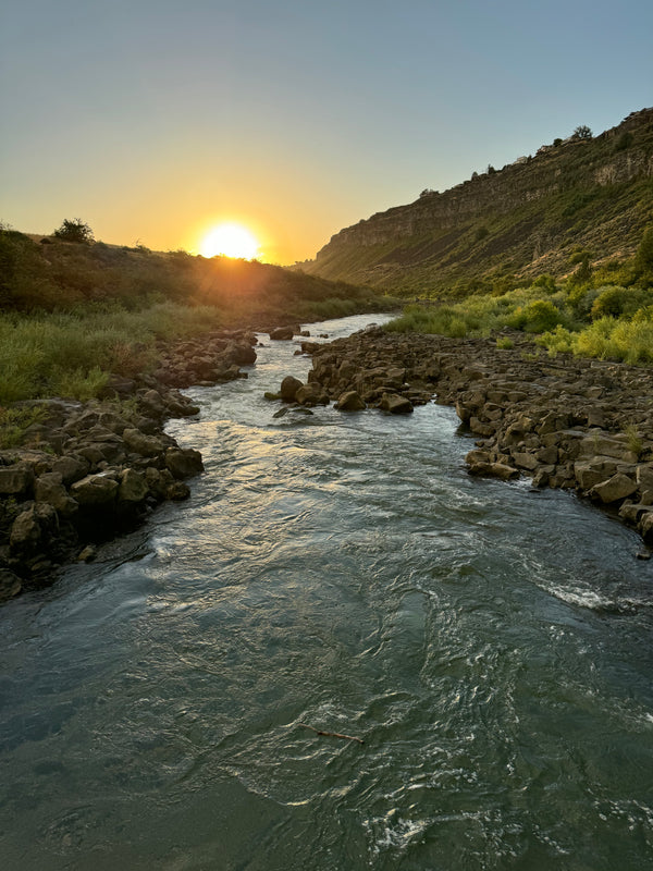 Stream flowing through a rocky landscape with a sunset in the background